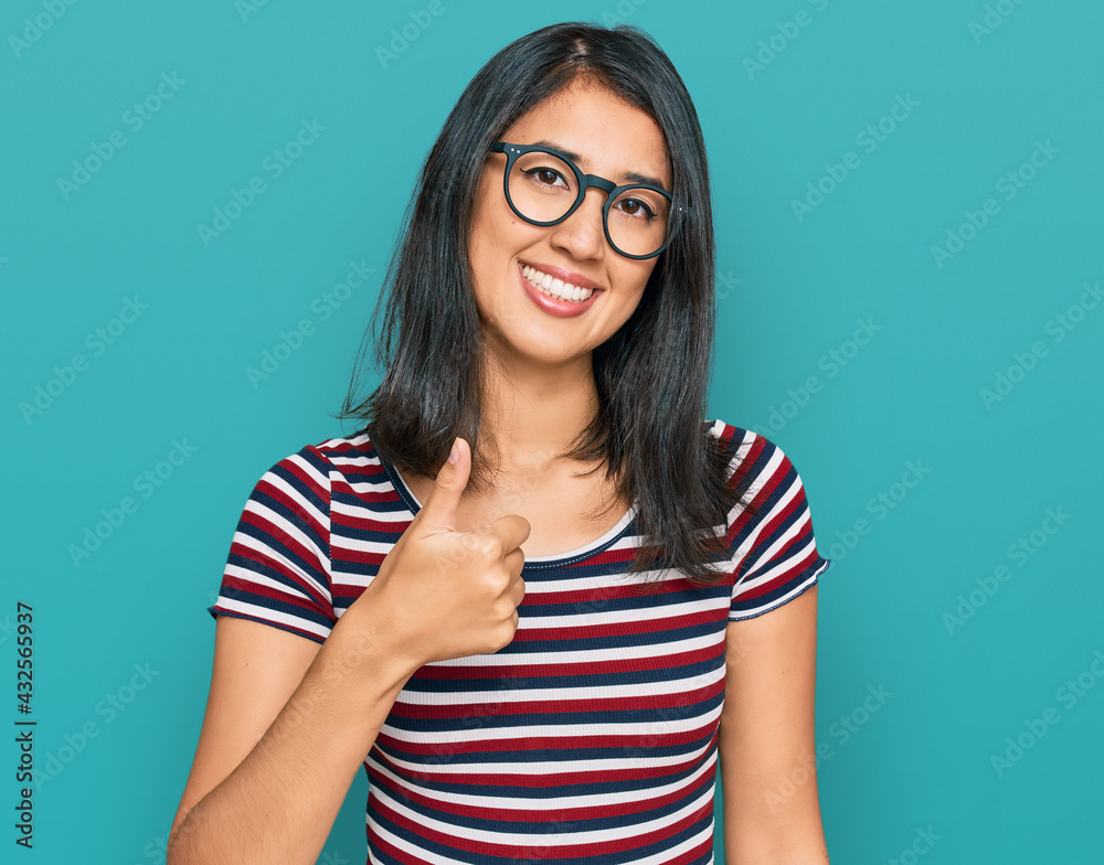Beautiful asian young woman wearing casual clothes and glasses doing happy thumbs up gesture with hand. approving expression looking at the camera showing success. Beautiful asian young woman wearing casual clothes and glasses doing happy thumbs up gesture with hand. approving expression looking at the camera showing success.