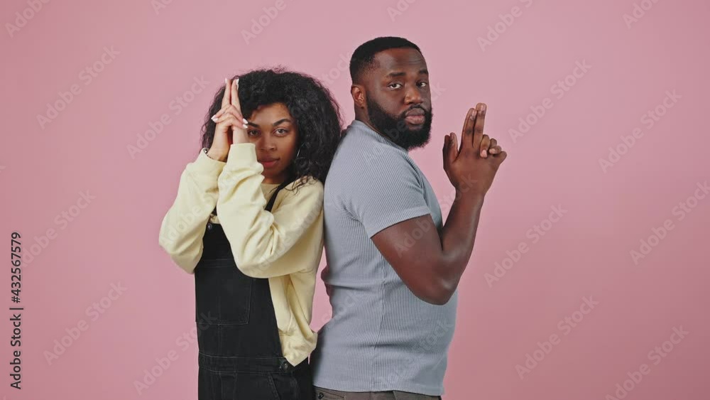 African american man and woman posing back to back, holding hands like guns and shooting to camera, violet background African american man and woman posing back to back, holding hands like guns and shooting to camera, violet background