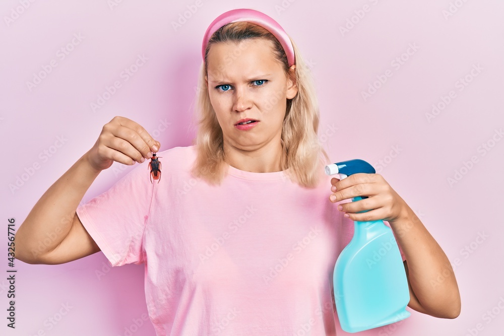 Beautiful caucasian blonde woman holding cockroach and pesticide sprayer clueless and confused expression. doubt concept. Beautiful caucasian blonde woman holding cockroach and pesticide sprayer clueless and confused expression. doubt concept.