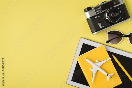 Top view photo of camera sunglasses tablet computer plane model yellow pencil and notebook on isolated pastel yellow background with copyspace