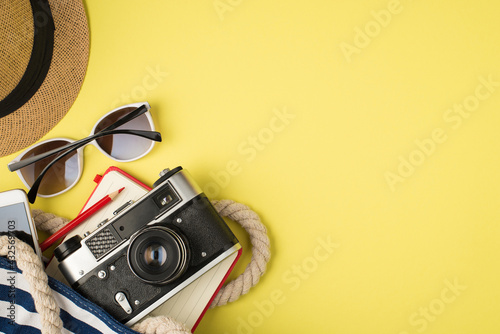 Overhead photo of hat sunglasses phone bag camera notebook and pencil isolated on the yellow background with empty space