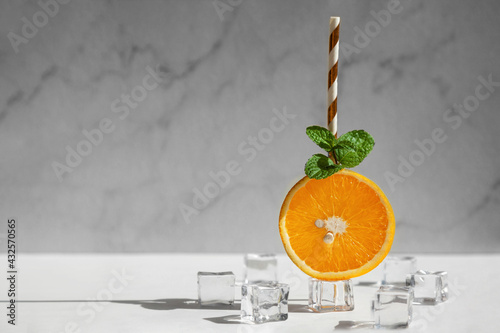 Orange slice with leaf of mintand a straw on cube of ice. Citrus ship on ice. Concept of cold summer drink. photo