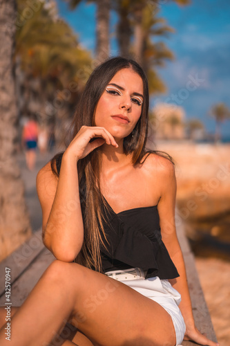 Summer lifestyle, portrait of a brunette Caucasian in short pants and black t-shirt on the Mediterranean coast sitting by the sea © unai