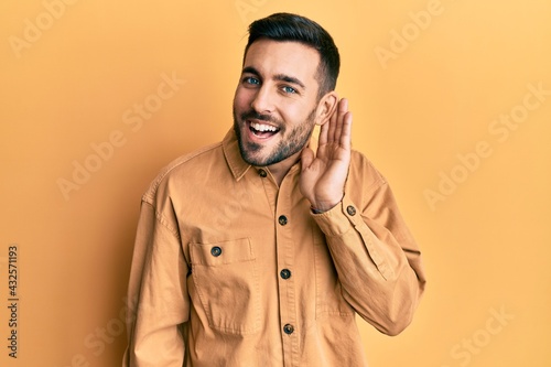 Young hispanic man wearing casual clothes smiling with hand over ear listening and hearing to rumor or gossip. deafness concept.
