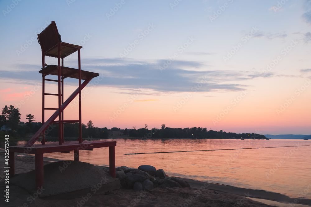 Silhouette of an empty red lifeguard chair during idyllic sunset or sunrise at Lamure Beach along the Ottawa River at Deep River, Ontario Canada.