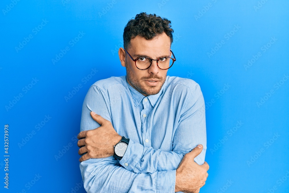 Young hispanic man wearing casual clothes and glasses shaking and freezing for winter cold with sad and shock expression on face Young hispanic man wearing casual clothes and glasses shaking and freezing for winter cold with sad and shock expression on face