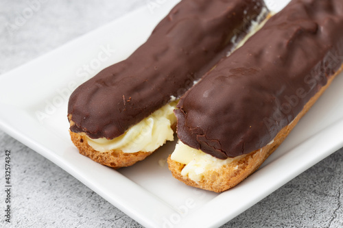 Chocolate eclair with a custard cream filling on a white plate. With a concrete background