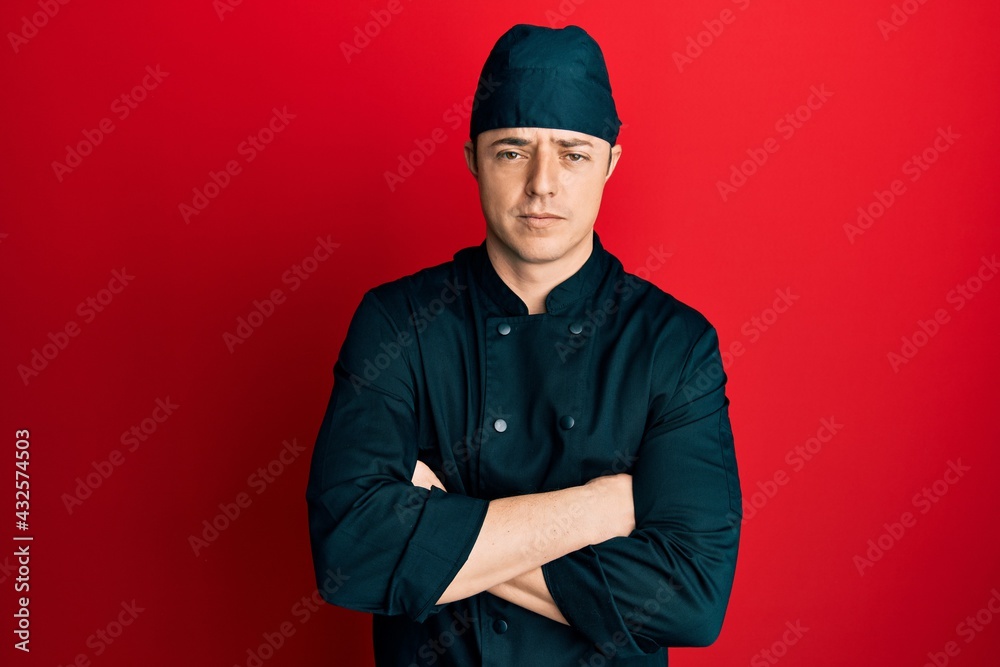 Handsome young man wearing professional cook uniform and hat skeptic and nervous, disapproving expression on face with crossed arms. negative person. Handsome young man wearing professional cook uniform and hat skeptic and nervous, disapproving expression on face with crossed arms. negative person.