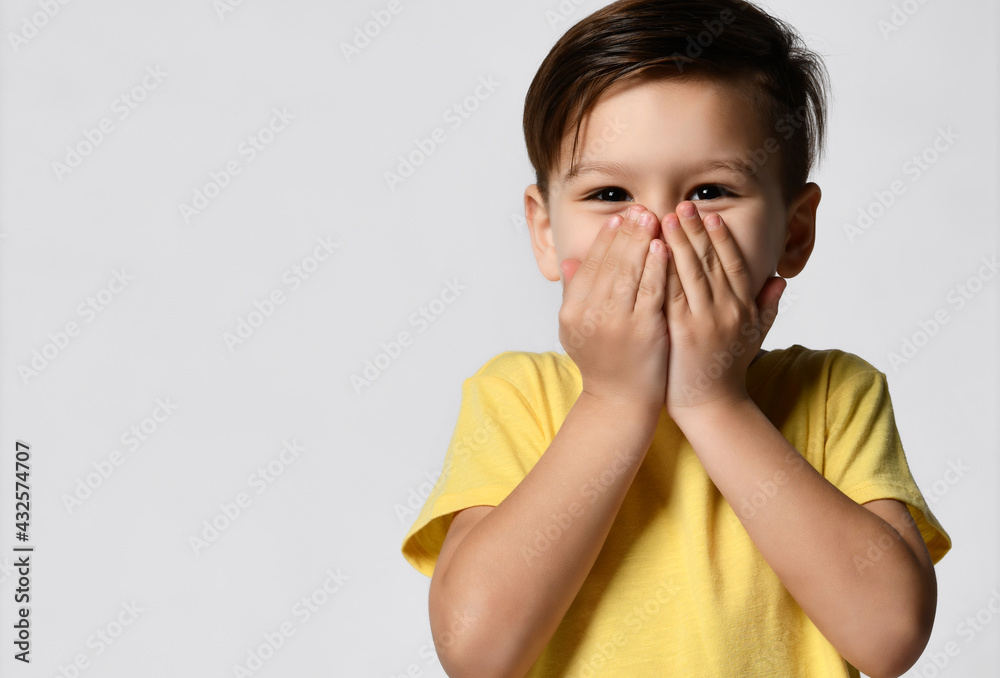 Studio shot of cheerful beautiful european preschooler kid covering her mouth with both hands, giggling, laughing at a joke, looking shyly, suppressing laughter Studio shot of cheerful beautiful european preschooler kid covering her mouth with both hands, giggling, laughing at a joke, looking shyly, suppressing laughter