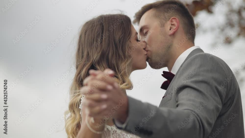 Newlyweds. Lovely young caucasian bride and groom holding hands. Wedding happy family couple making a kiss on mountain slope hill. Man and woman in love. Autumn tree. Bride in gorgeous wedding dress