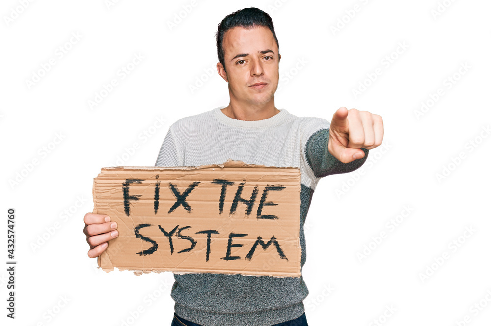 Handsome young man holding fix the system banner cardboard pointing with finger to the camera and to you, confident gesture looking serious Handsome young man holding fix the system banner cardboard pointing with finger to the camera and to you, confident gesture looking serious