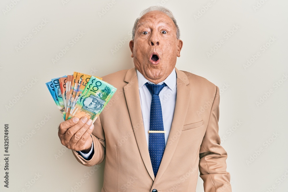 Senior caucasian man holding australian dollars scared and amazed with open mouth for surprise, disbelief face Senior caucasian man holding australian dollars scared and amazed with open mouth for surprise, disbelief face