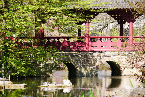 covered japanese stone bridge with red wooden railings in the sunlight over a river
