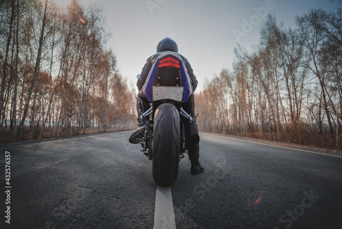 A motorbiker is ready to ride on the asphalt road. Rear view.