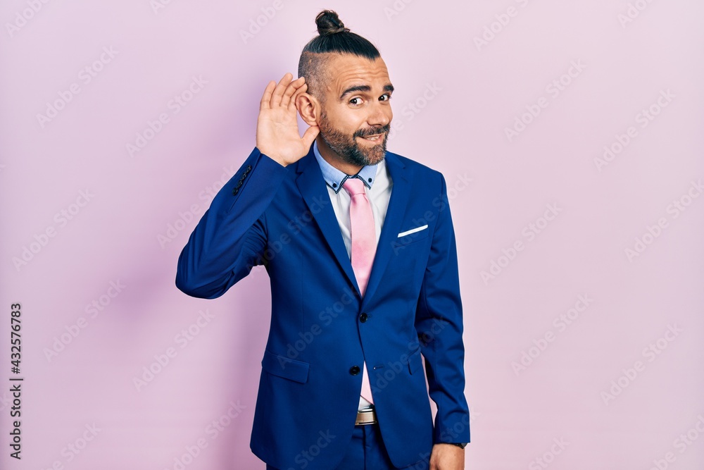Young hispanic man wearing business suit and tie smiling with hand over ear listening an hearing to rumor or gossip. deafness concept. Young hispanic man wearing business suit and tie smiling with hand over ear listening an hearing to rumor or gossip. deafness concept.