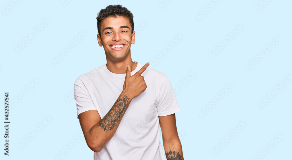 Young handsome african american man wearing casual white tshirt cheerful with a smile of face pointing with hand and finger up to the side with happy and natural expression on face Young handsome african american man wearing casual white tshirt cheerful with a smile of face pointing with hand and finger up to the side with happy and natural expression on face