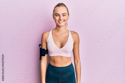 Beautiful blonde woman wearing sportswear and arm band with a happy and cool smile on face. lucky person. © Krakenimages.com