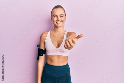 Beautiful blonde woman wearing sportswear and arm band smiling friendly offering handshake as greeting and welcoming. successful business. © Krakenimages.com