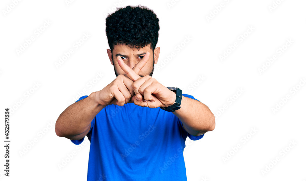 Young arab man with beard wearing casual blue t shirt rejection expression crossing fingers doing negative sign Young arab man with beard wearing casual blue t shirt rejection expression crossing fingers doing negative sign