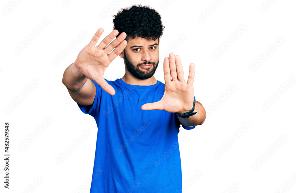Young arab man with beard wearing casual blue t shirt doing frame using hands palms and fingers, camera perspective Young arab man with beard wearing casual blue t shirt doing frame using hands palms and fingers, camera perspective