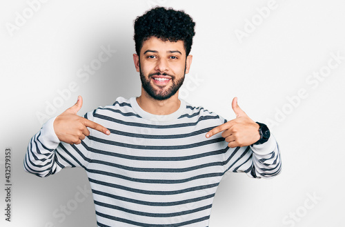 Young arab man with beard wearing casual striped sweater looking confident with smile on face  pointing oneself with fingers proud and happy.