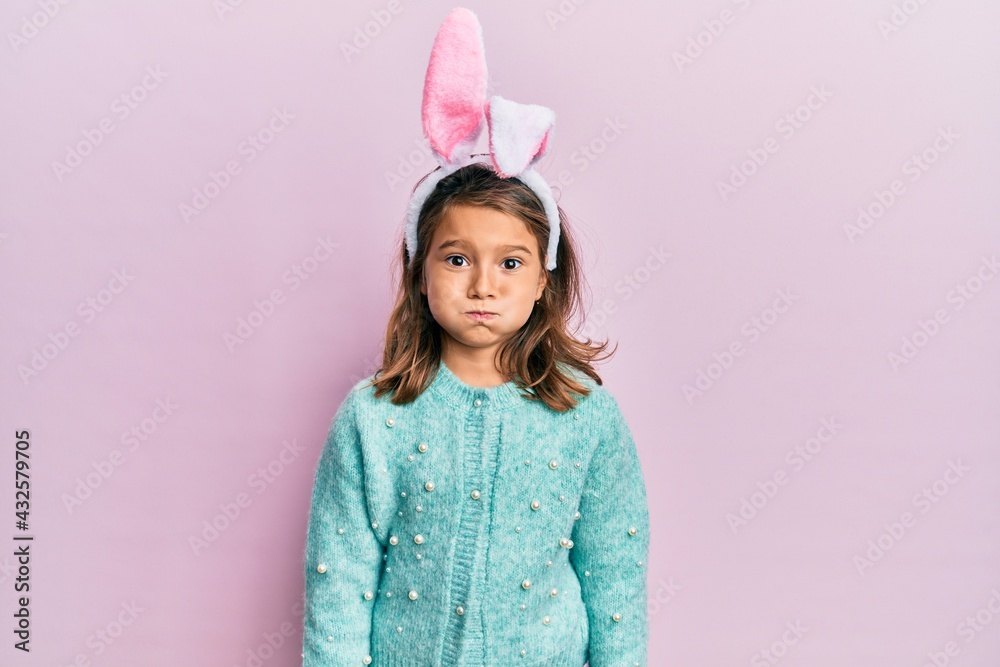 Little beautiful girl wearing cute easter bunny ears puffing cheeks with funny face. mouth inflated with air, crazy expression.
