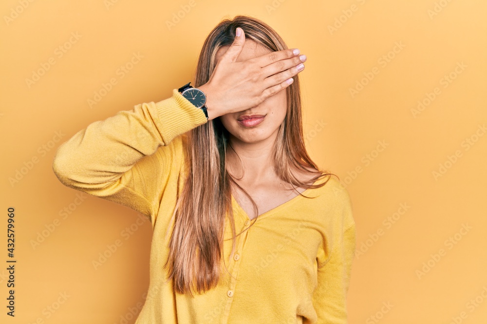 Beautiful hispanic woman wearing casual yellow sweater covering eyes with hand, looking serious and sad. sightless, hiding and rejection concept