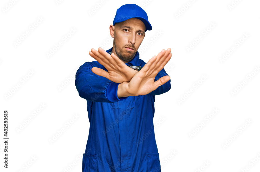 Bald man with beard wearing builder jumpsuit uniform rejection expression crossing arms and palms doing negative sign, angry face Bald man with beard wearing builder jumpsuit uniform rejection expression crossing arms and palms doing negative sign, angry face