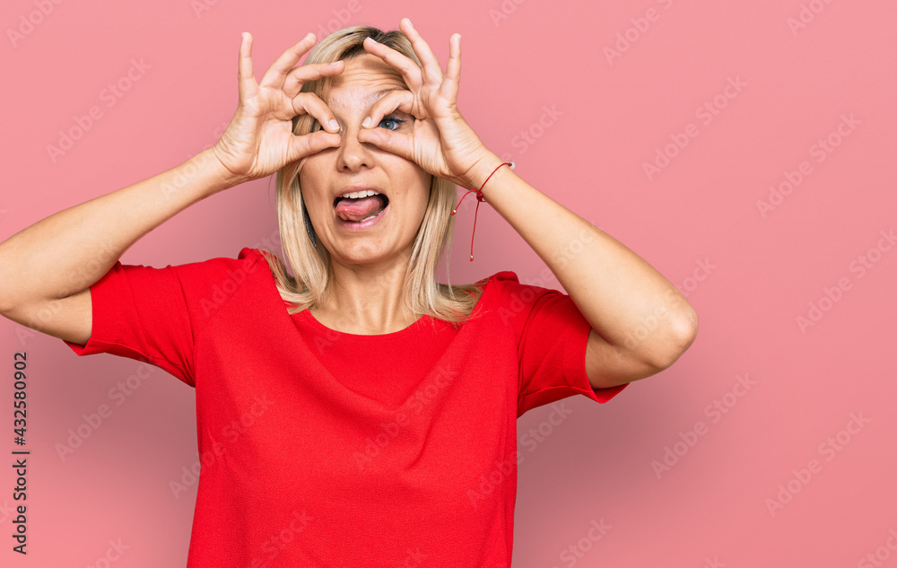 Middle age caucasian woman wearing casual clothes doing ok gesture like binoculars sticking tongue out, eyes looking through fingers. crazy expression.