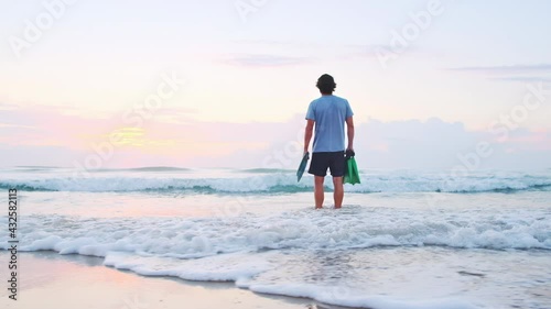 Bodysurfer. Young male bodysurfer stands on the beach with fins and handplane and checks the waves at sunrise photo