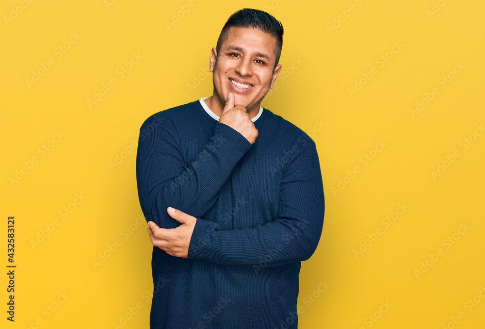 Young latin man wearing casual clothes looking confident at the camera with smile with crossed arms and hand raised on chin. thinking positive. Young latin man wearing casual clothes looking confident at the camera with smile with crossed arms and hand raised on chin. thinking positive.