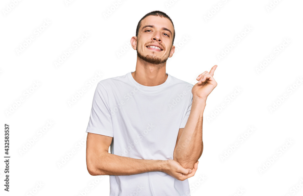 Hispanic young man wearing casual white t shirt with a big smile on face, pointing with hand and finger to the side looking at the camera. Hispanic young man wearing casual white t shirt with a big smile on face, pointing with hand and finger to the side looking at the camera.