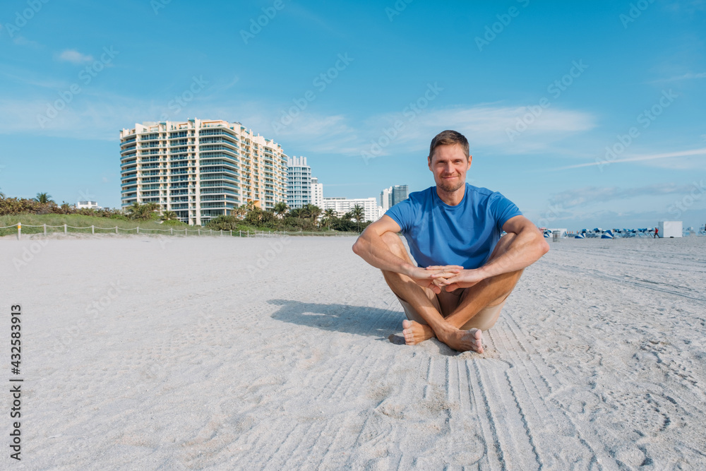 Guy walking along the empty sandy Miami beach. Happy handsome man tourist in casual clothes sitting on sandy beach. Travel and tourism concept.