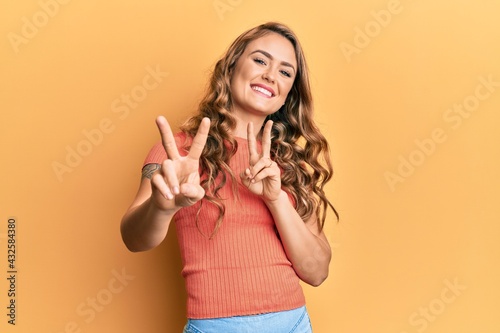 Young blonde girl wearing casual clothes smiling looking to the camera showing fingers doing victory sign. number two.