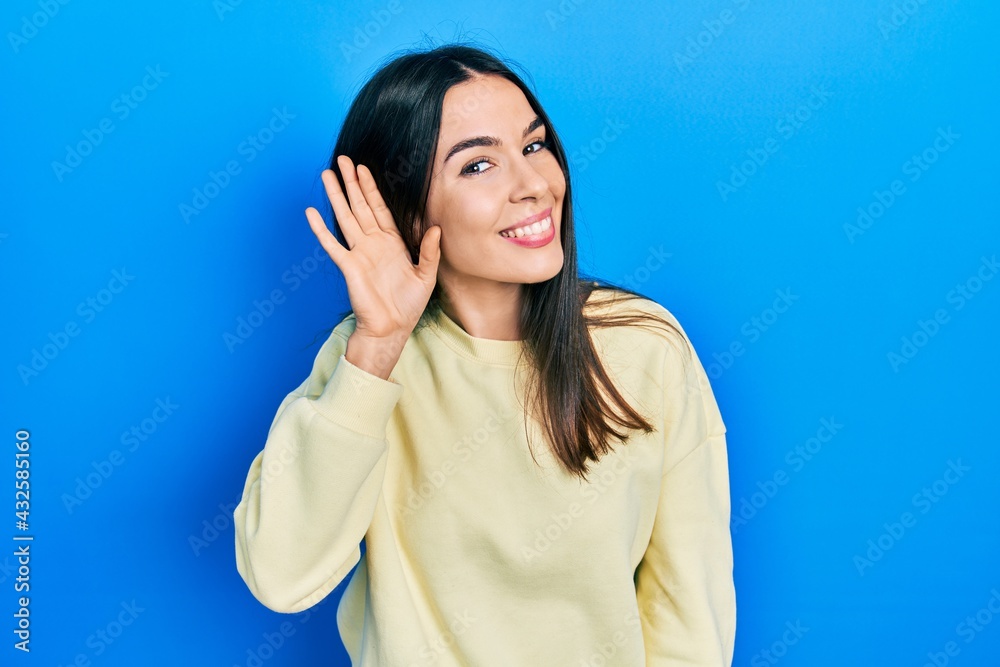 Fototapeta premium Young brunette woman wearing casual sweatshirt smiling with hand over ear listening an hearing to rumor or gossip. deafness concept.