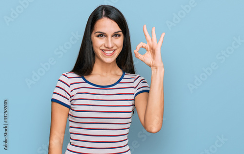 Young hispanic girl wearing casual striped t shirt smiling positive doing ok sign with hand and fingers. successful expression.