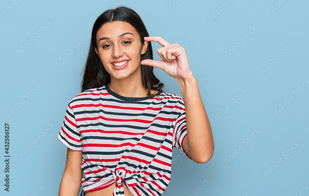 Young hispanic girl wearing casual clothes smiling and confident gesturing with hand doing small size sign with fingers looking and the camera. measure concept. Young hispanic girl wearing casual clothes smiling and confident gesturing with hand doing small size sign with fingers looking and the camera. measure concept.