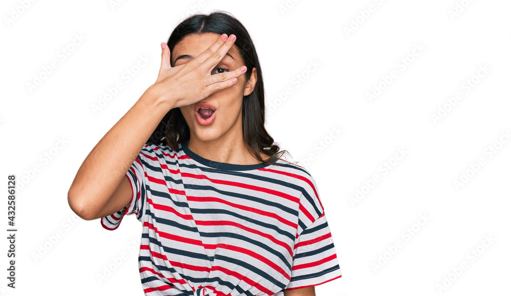 Young hispanic girl wearing casual clothes peeking in shock covering face and eyes with hand, looking through fingers with embarrassed expression. Young hispanic girl wearing casual clothes peeking in shock covering face and eyes with hand, looking through fingers with embarrassed expression.