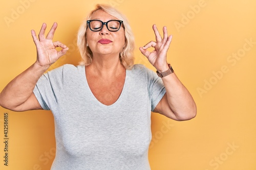 Middle age blonde woman wearing casual clothes and glasses relax and smiling with eyes closed doing meditation gesture with fingers. yoga concept.