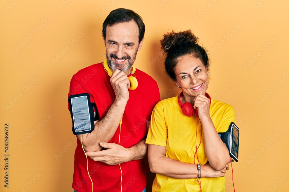 Middle age couple of hispanic woman and man wearing sportswear and arm band looking confident at the camera with smile with crossed arms and hand raised on chin. thinking positive.