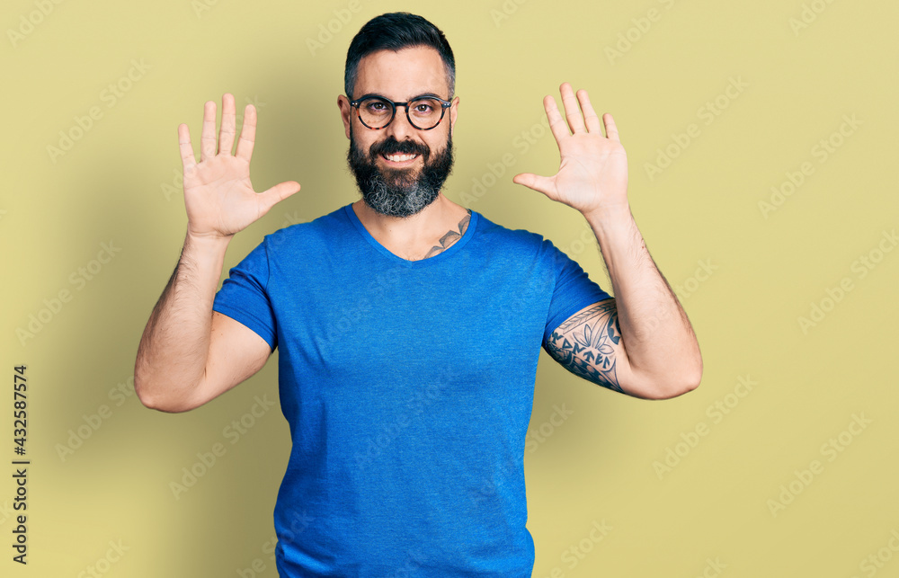Hispanic man with beard wearing casual t shirt and glasses showing and pointing up with fingers number ten while smiling confident and happy. Hispanic man with beard wearing casual t shirt and glasses showing and pointing up with fingers number ten while smiling confident and happy.
