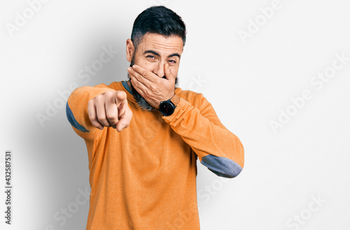 Hispanic man with beard wearing casual winter sweater laughing at you, pointing finger to the camera with hand over mouth, shame expression