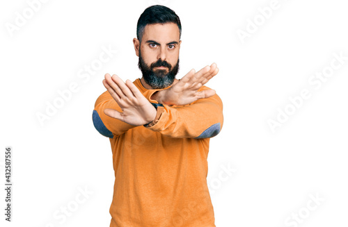 Hispanic man with beard wearing casual winter sweater rejection expression crossing arms and palms doing negative sign, angry face