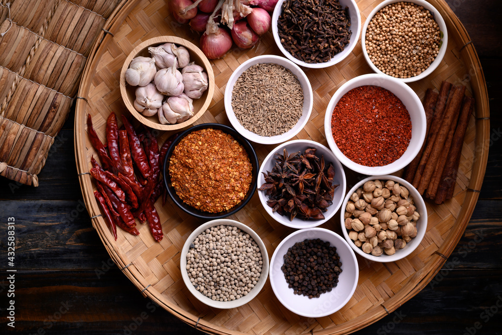 Various dry spices and herbs in a bowl on bamboo tray. Asian food ingredients (chili, clove, caraway, coriander seed, star anise, cardamom, pepper, cinnamon, garlic and shallot)