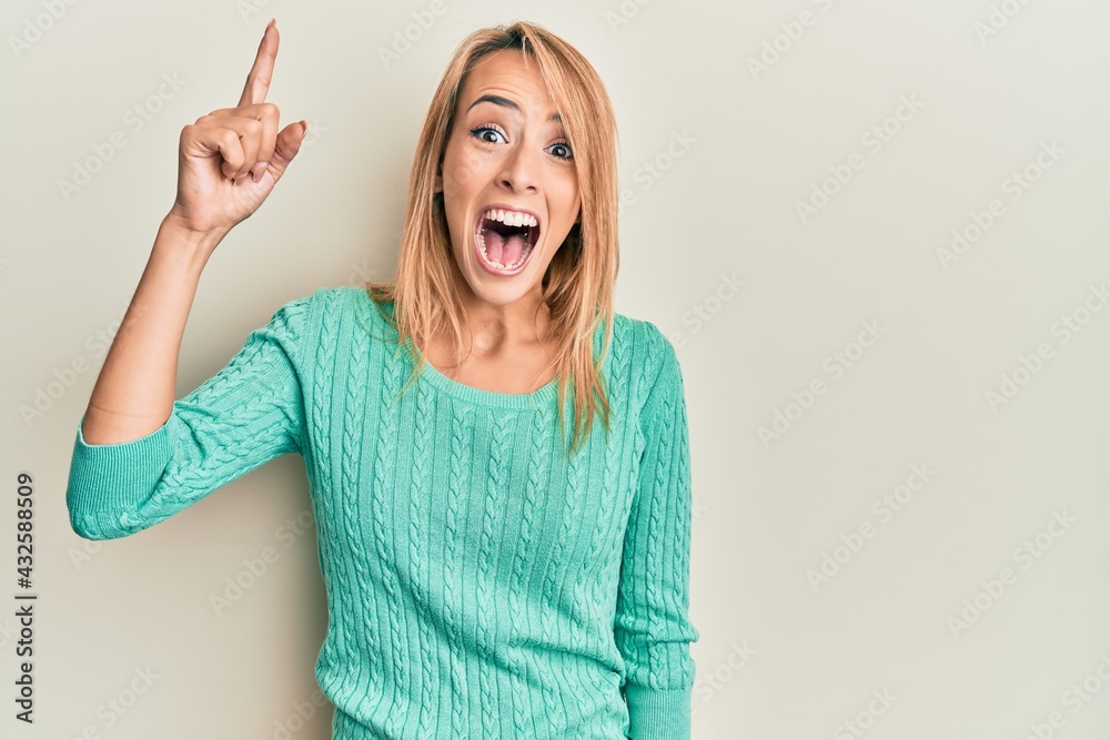 Beautiful blonde woman wearing casual winter sweater pointing finger up with successful idea. exited and happy. number one. Beautiful blonde woman wearing casual winter sweater pointing finger up with successful idea. exited and happy. number one.
