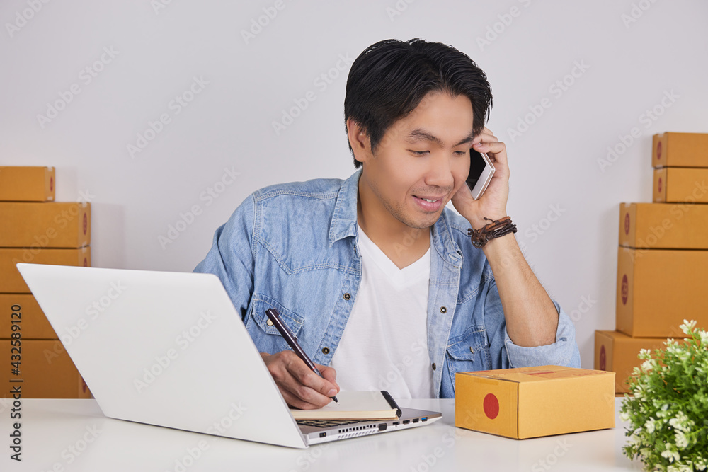 Online Merchant or Casual Businessman in Online Store Using Smartphone and Writing Note and See Customer Address on Parcel or Package Online Merchant or Casual Businessman in Online Store Using Smartphone and Writing Note and See Customer Address on Parcel or Package