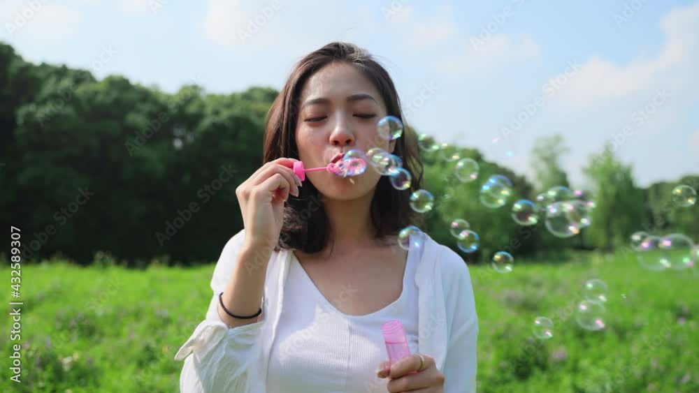 4k slow motion of Young beautiful Asian girl in white shirt blowing bubbles on the grass spring field under blue sky relax freedom concept 4k slow motion of Young beautiful Asian girl in white shirt blowing bubbles on the grass spring field under blue sky relax freedom concept