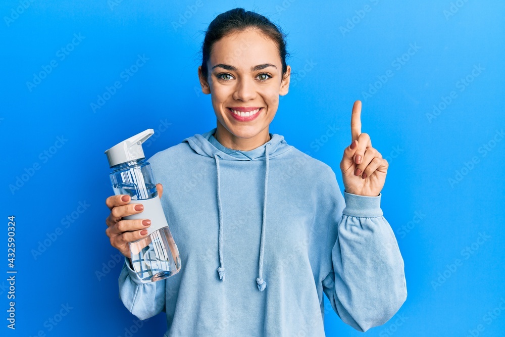 Young caucasian blonde woman drinking bottle of water smiling with an idea or question pointing finger with happy face, number one Young caucasian blonde woman drinking bottle of water smiling with an idea or question pointing finger with happy face, number one