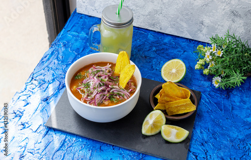 Dish of encebollado, typical Ecuadorian food prepared with fish, onion and yucca on a blue background next to a window. photo