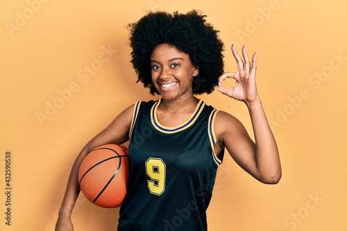 Young african american woman holding basketball ball doing ok sign with fingers, smiling friendly gesturing excellent symbol